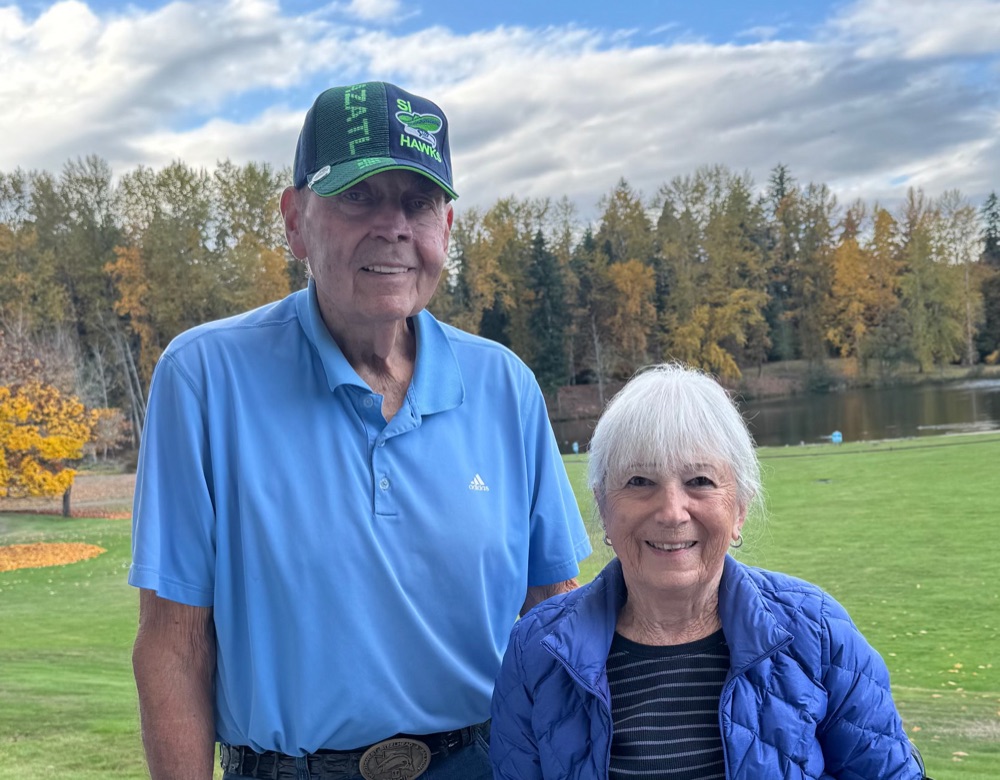Larry and Dian Olson standing outdoors in front of a lake and fall trees
